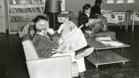 Black & White photo, four people sitting in the library and reading the newspapers