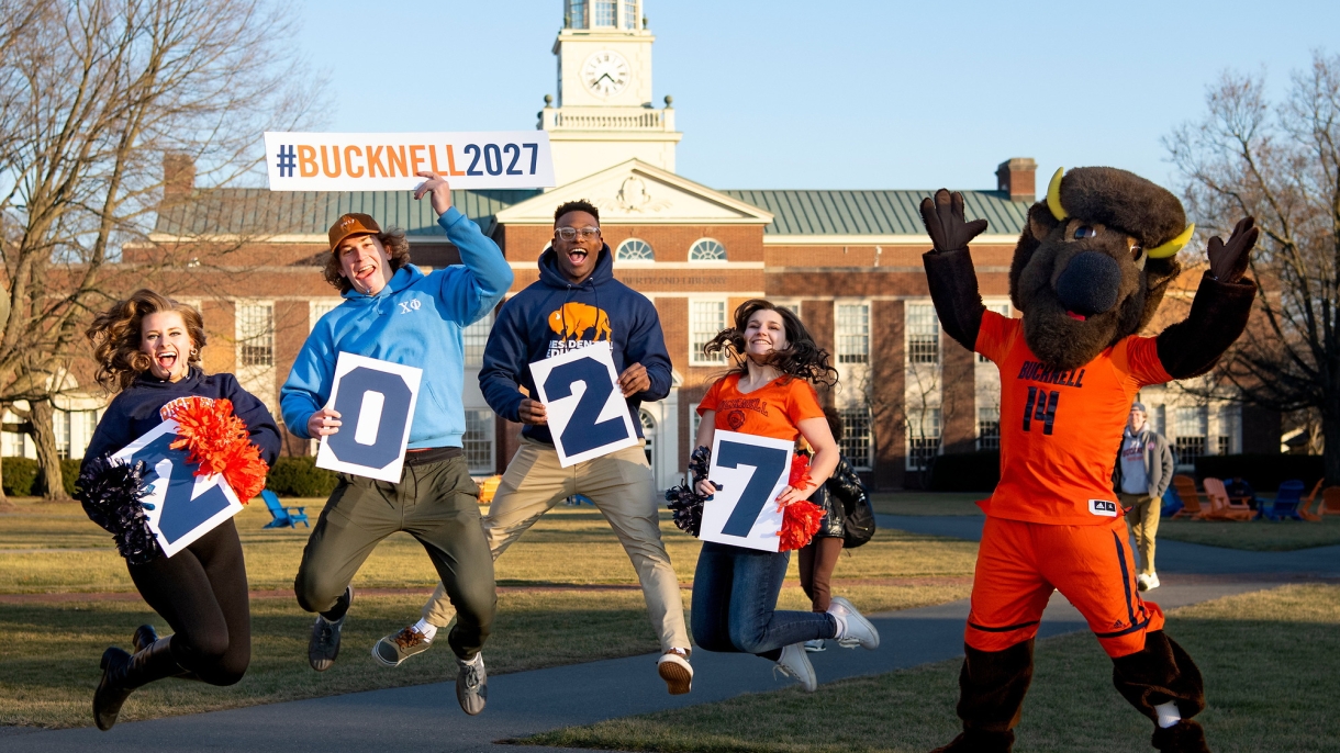 Students and Bucky jumping on Malesardi Quad holding signs welcoming the class of 2027