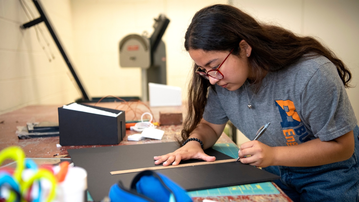 Cindy Cortez uses a ruler to draw a straight line on a piece of black material.