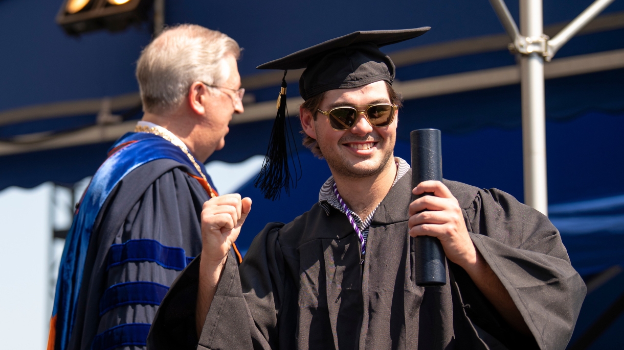 Graduate wearing a cap and gown celebrates getting his diploma.