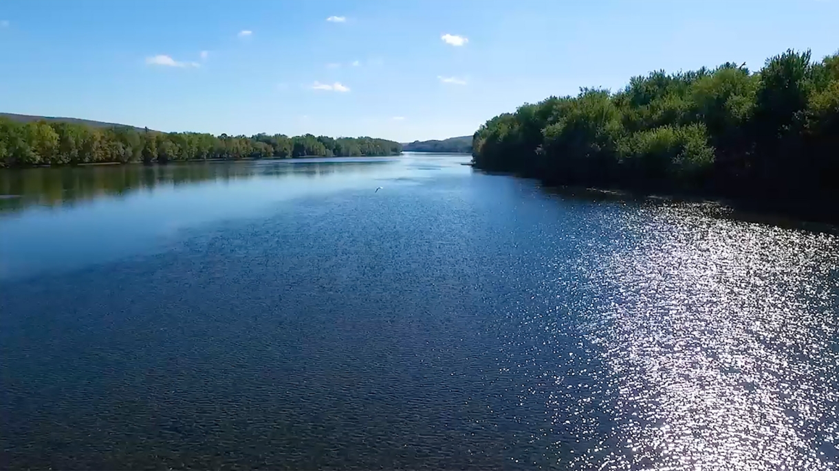 Calm river with blue sky and sun on water.