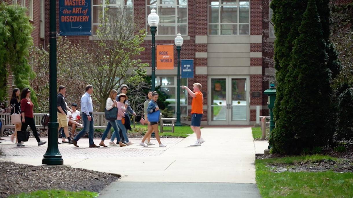 Students standing on sidewalk outside. 