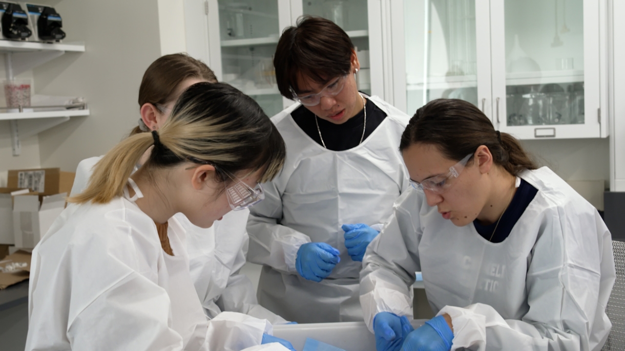 Students in lab gear observe experiment together