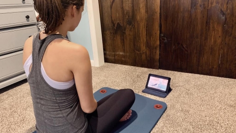 A student sits on a yoga mat in front of a tablet.