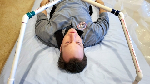 Professor Brandon Vogel lies under the frame of a prototype intubation tent.