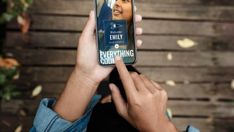 A woman&#039;s hand holds a smartphone with a Bucknell custom viewbook displayed on screen as she points with her other hand