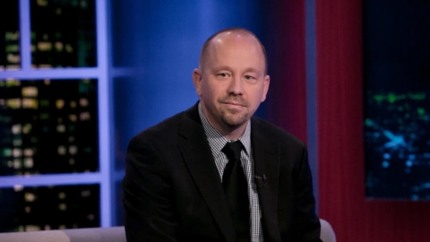 professor Jon A. Shields sits in a chair, dressed in a black suit