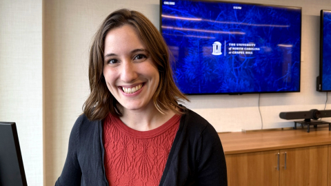 Juliet King smiles in a room where a large screen is on the wall behind her with the University of North Carolina's logo