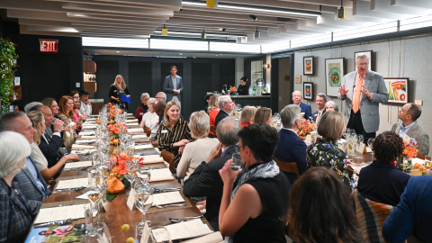 A large group sits at tables having a meal.