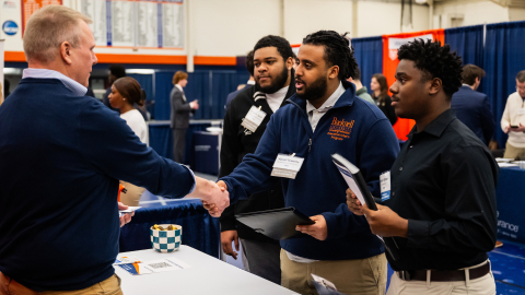 Students at a career fair shake hands with an employer