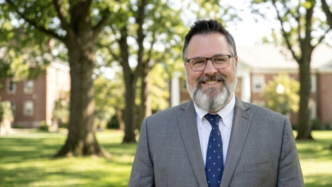 Portrait of Sean Schofield wearing a suit outdoors surrounded by trees.