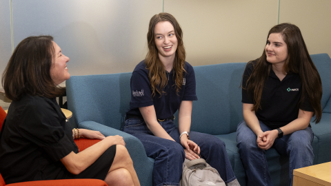 Three women sit on a couch while talking about their shared alumni connection.