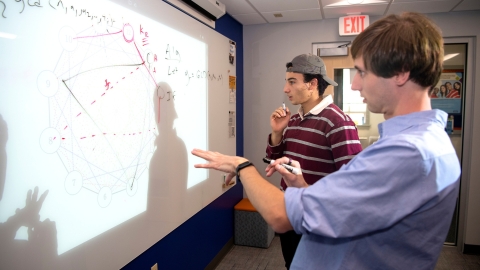 Sam Gutekunst stands at a whiteboard with a student