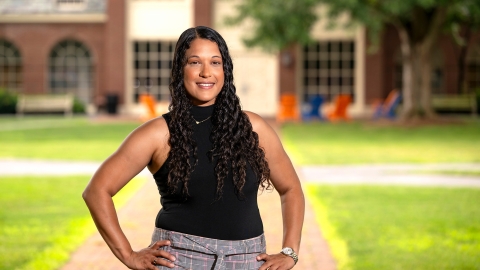 Jasmine Jones &#039;25 stands on campus on a brick walkway with green grass on both sides of it, with her hands on her hips and smiling.