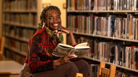 Athaliah Elvis smiles with an open book in her hand and book stacks in the background.