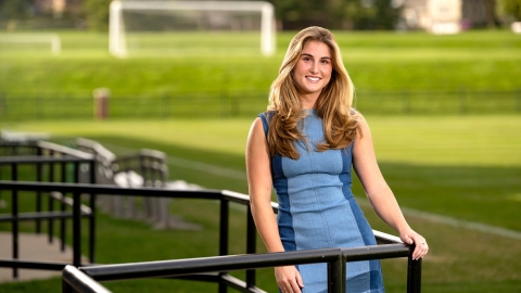 Lea Tarzy '24 poses in a blue dress in the stands of a soccer field.