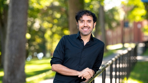 Portrait of Eddy Lopez leaning on a railing outdoors in a wooded area.