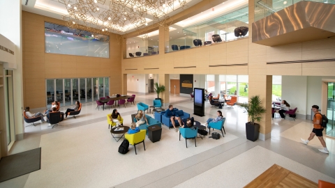 A down angle photograph of students walking and sitting in the lobby of Holmes Hall.