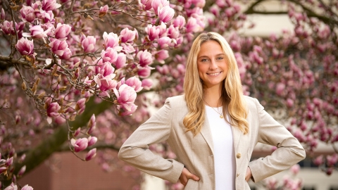 Abigail Kates &#039;24 stands with her hands on her hips and smiles, cherry blossoms are in the background