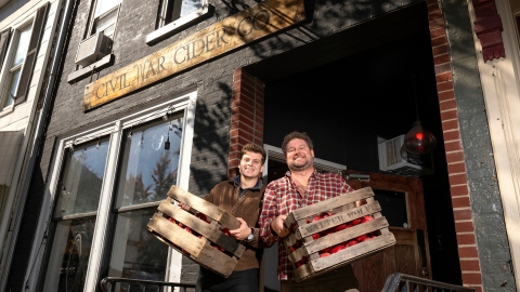 Ben Fink and Rob Antanitis hold crates of apples outside Civil War Cider.