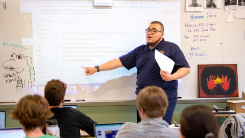 Christian Melgar '23 points to a whiteboard in front of a room of students.