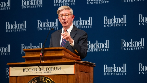 George Will speaks from a podium with a &quot;Bucknell Forum&quot; plaque.