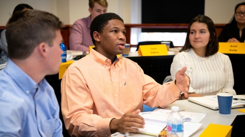 A student asks a question in a management class as two other students look on