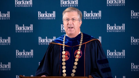 President John Bravman speaks at podium dressed in regalia