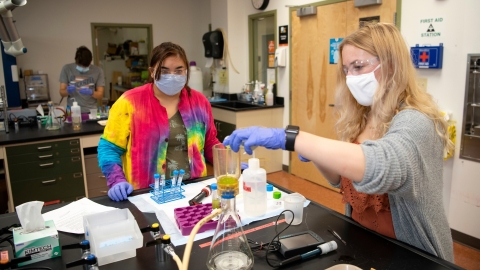 Jackie Zak pumps liquid into a vial with a pipette as Leah Henk watches