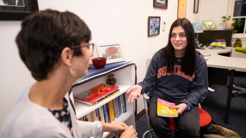 Professor Elena Machado and Emily Sanchez '23 talk in a faculty office, Sanchez holding a book