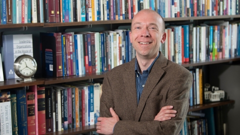 Scott Meinke poses for portrait in front of bookshelf