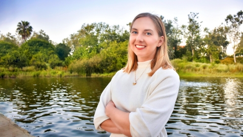 Christina Sfedu &#039;12 stands with her arms crossed in front of a lake.