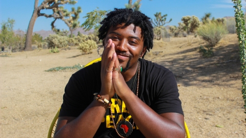 Michael Tonge sits with his hands folded in front of his face and a desert landscape in the background