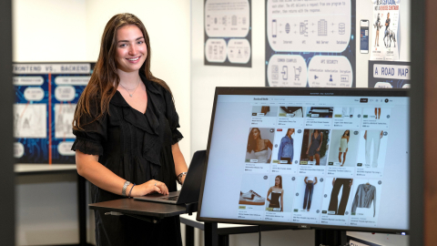 Ava Sklar smiles beside a monitor displaying clothing listings on her Bucknell Refit website.