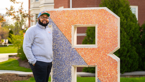 Jawaad "KJ" Benson stands next to a large letter B that is part blue and part orange.