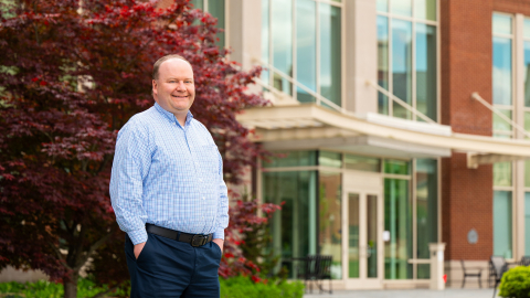 Joe Wilck stands with his hands in his pockets and smiles outside of Holmes Hall.