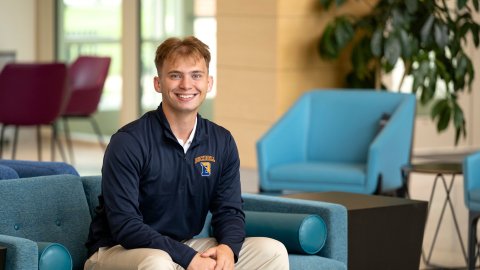 Kaleb Eger sits on a teal chair and smiles.