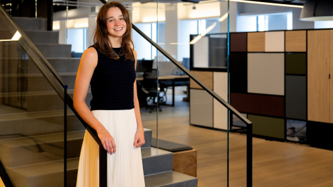Kelly Byrne stands at the bottom of a staircase with an office scene in the background.