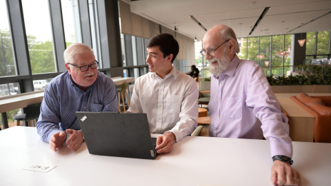 Max Quan is working on a laptop in an office setting with David Hamill to his right and Jack Hoadley to his left.