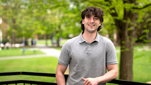 Michael Evanick stands outdoors on campus and smiles; green grass and trees are behind him.
