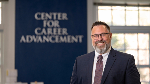 Sean Schofield poses in a suit before a sign that says "Center for Career Advancement"