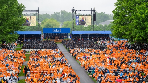 Rows of seniors sit facing the Commencement platform, many dressed in orange ponchos due to rain, at the 2024 Commencement.