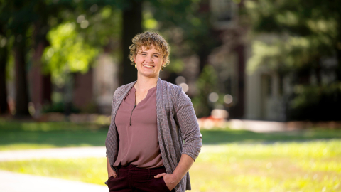 Annie Ross smiles with her hands in her pockets with greenery in the background.