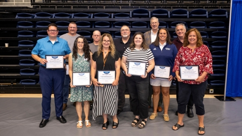 10 employees stand with John Bravman and smile while holding awards
