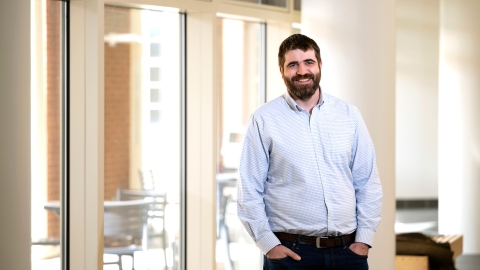 Professor Greg O'Neill wears a button-down shirt and stands and smiles with his hands in his pocket.s