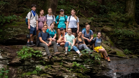 Many students sitting on a big rock formation. 