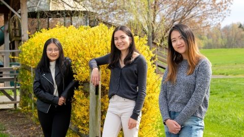 Three students standing in front of some landscaping.