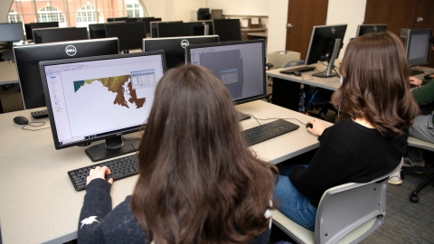 Two students sit and look at maps on their computer