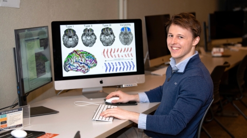 Will Snyder &#039;21 sits at desk with computers displaying brain scans