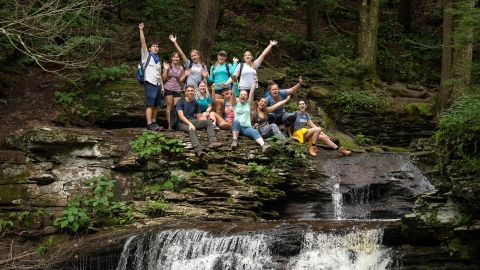 A group of students sit over a waterfall at Ricketts Glen during a pre-orientation hike